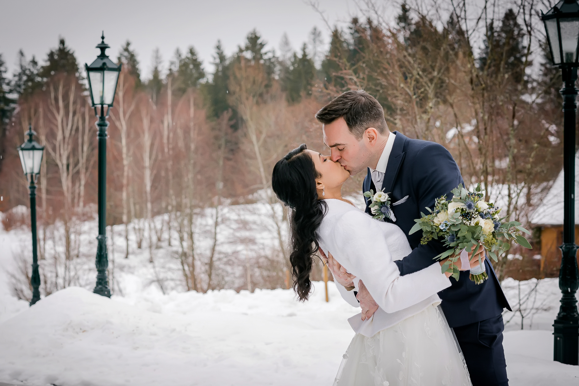 Winterhochzeit im Schwarzwald, das Brautpaar umarmt und küsst sich inmitten einer verschneiten Landschaft.