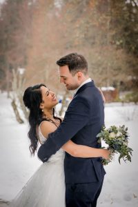 Ein verliebtes Brautpaar umarmt sich in einer traumhaften Schneelandschaft im Schwarzwald. Der Hintergrund ist von verschneiten Bäumen und Bergen geprägt, während das Paar im Mittelpunkt steht und glücklich in die Kamera schaut. Die talentierte Fotografin Isabela Campos hat diesen unvergesslichen Moment für die Ewigkeit festgehalten.