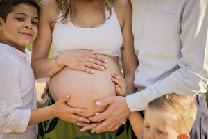 Ein wunderschönes Schwangerschaftsshooting mit Mama, Papa und den beiden Söhnen, bei dem das ungeborene Mädchen im Mittelpunkt steht. Die ganze Familie hält liebevoll ihre Hände auf den Bauch. Aufgenommen von der talentierten Fotografin Isabela Campos.