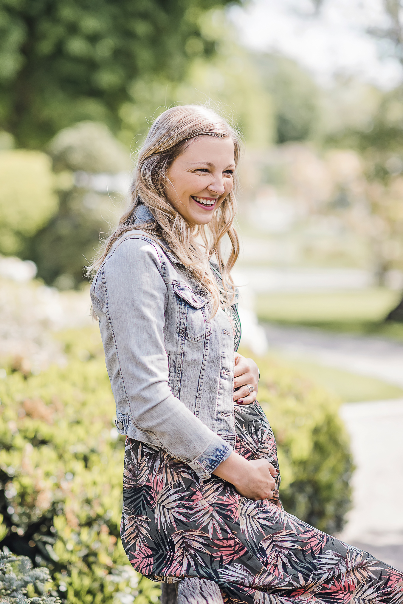 Schwangerschaft Fotoshooting in Freiburg im Park, blonde Schwangere hält ihren Babybauch und lacht