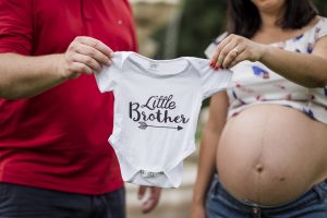Schwangerschaft Fotoshooting in Offenburg, Mama und Papa halten Body mit "Little Brother"