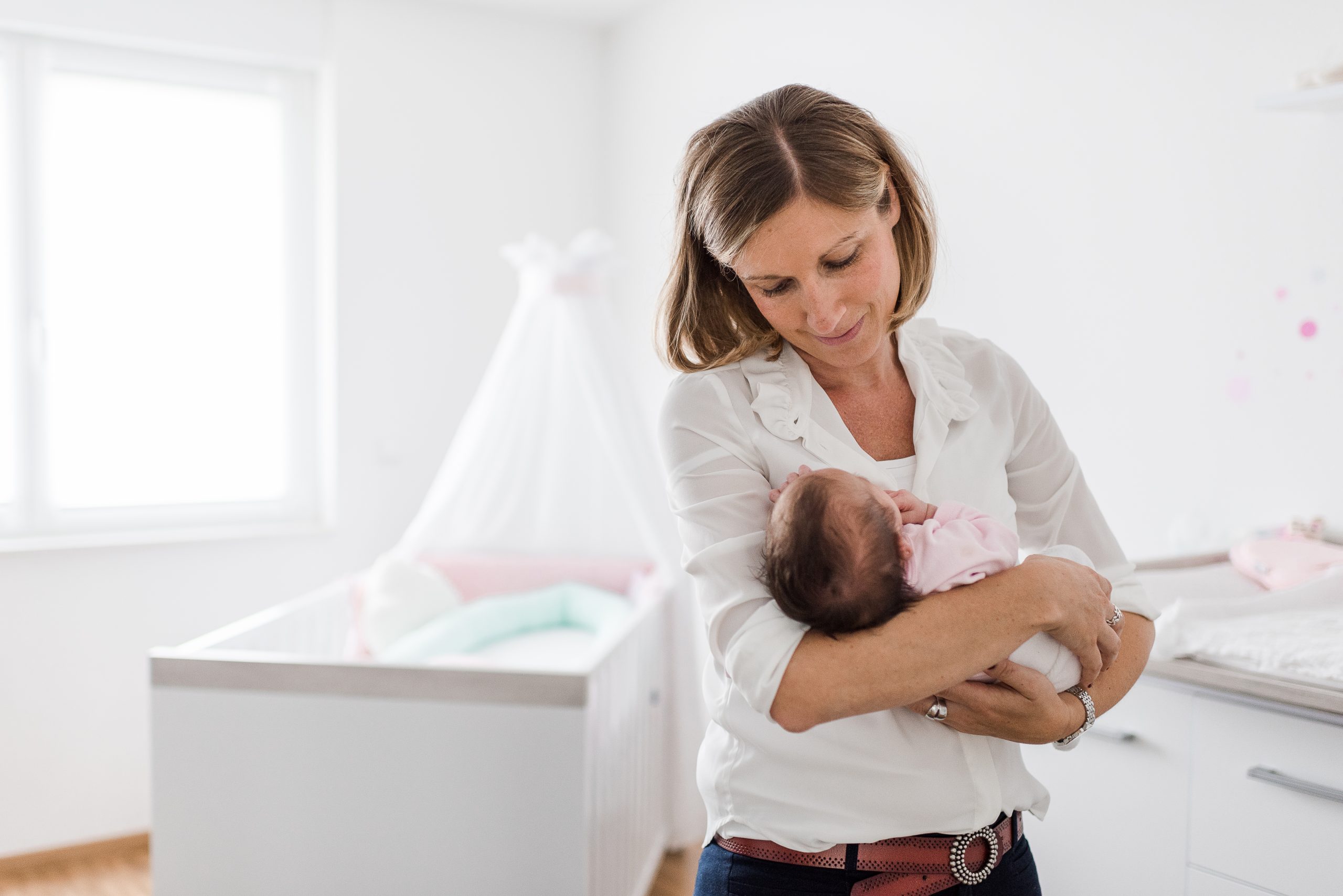 Newborn Fotoshooting in Freiburg - Mama hält Baby im Arm vor Hintergrund des Babyzimmers