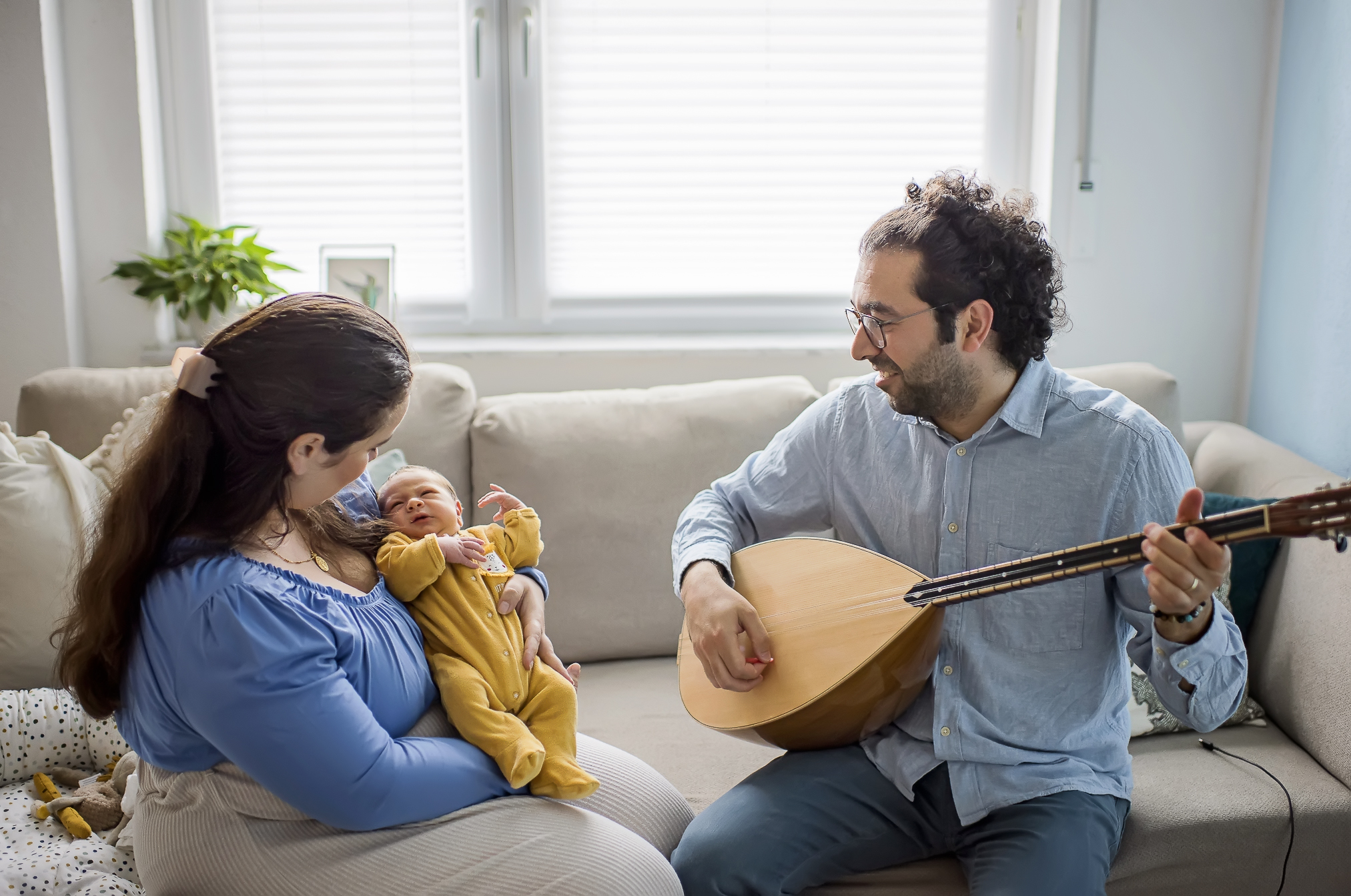 Newborn-Shooting im Wohnzimmer in Durbach, Mama hält das Baby und Papa spielt ein Instrument