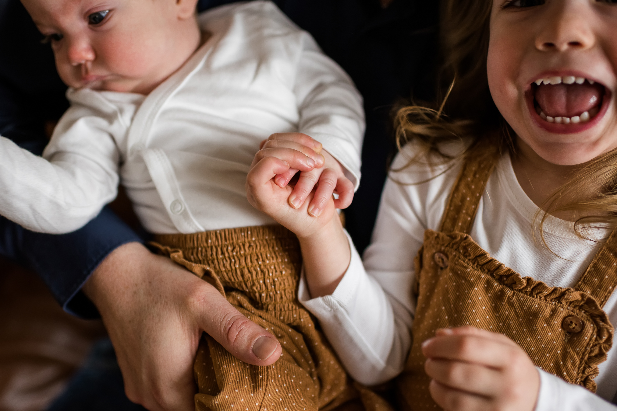 Newborn-Shooting mit großer Schwester zu Hause, Foto von ihrer Hand, die das Baby hält