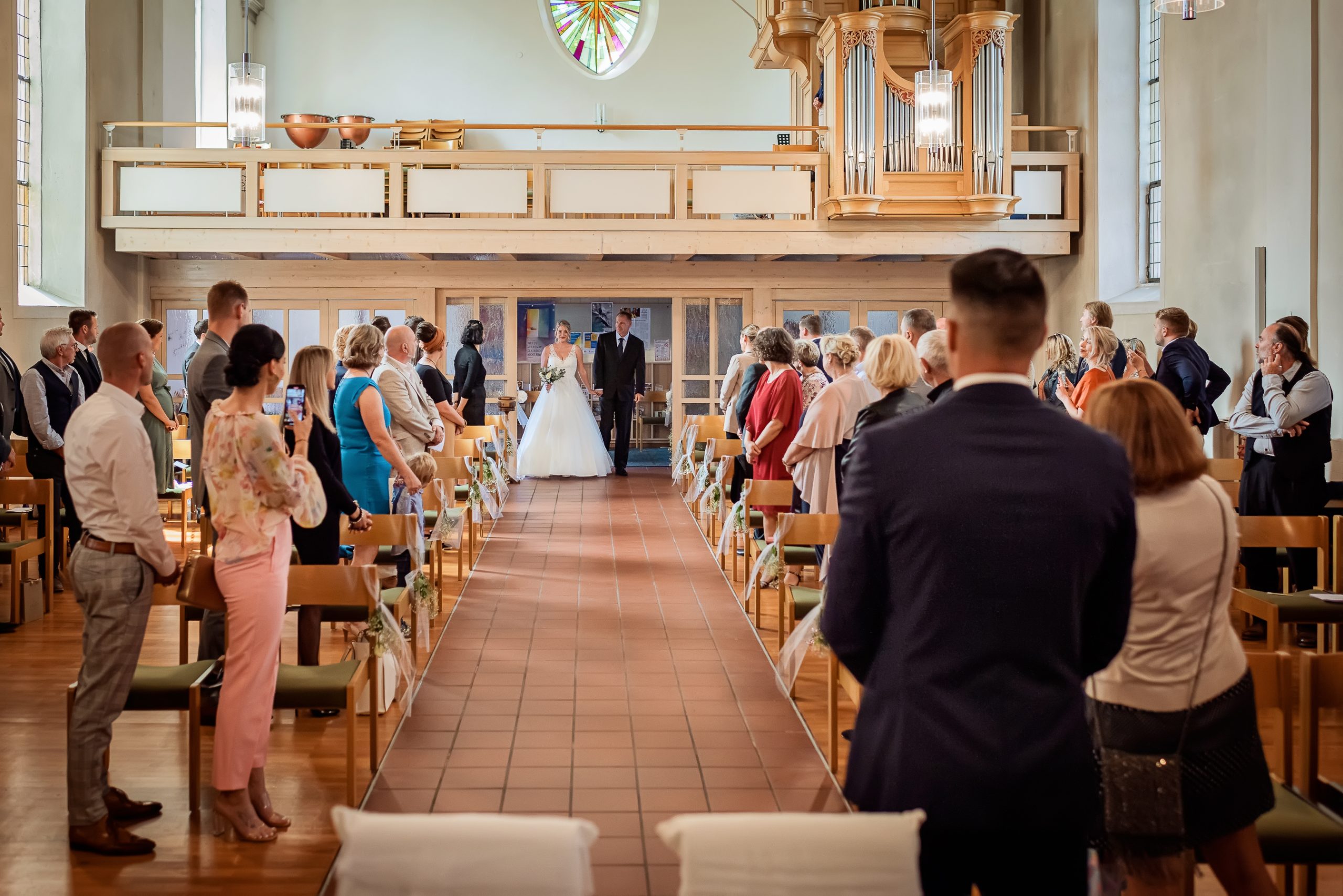 Ein Foto, das den Einzug der Braut in die Evangelische Kirche in Friesenheim während einer kirchlichen Hochzeit zeigt. Die Braut wird von ihrem Vater zum Altar geführt, während die Gäste ihre Blicke auf sie richten.