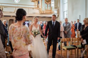 Ein Foto, das den bewegenden Moment der kirchlichen Hochzeit in der Evangelischen Kirche in Friesenheim zeigt. Das Bild fängt die Emotionen ein, als die Braut den Korridor entlangschreitet und der Bräutigam sie erwartet.