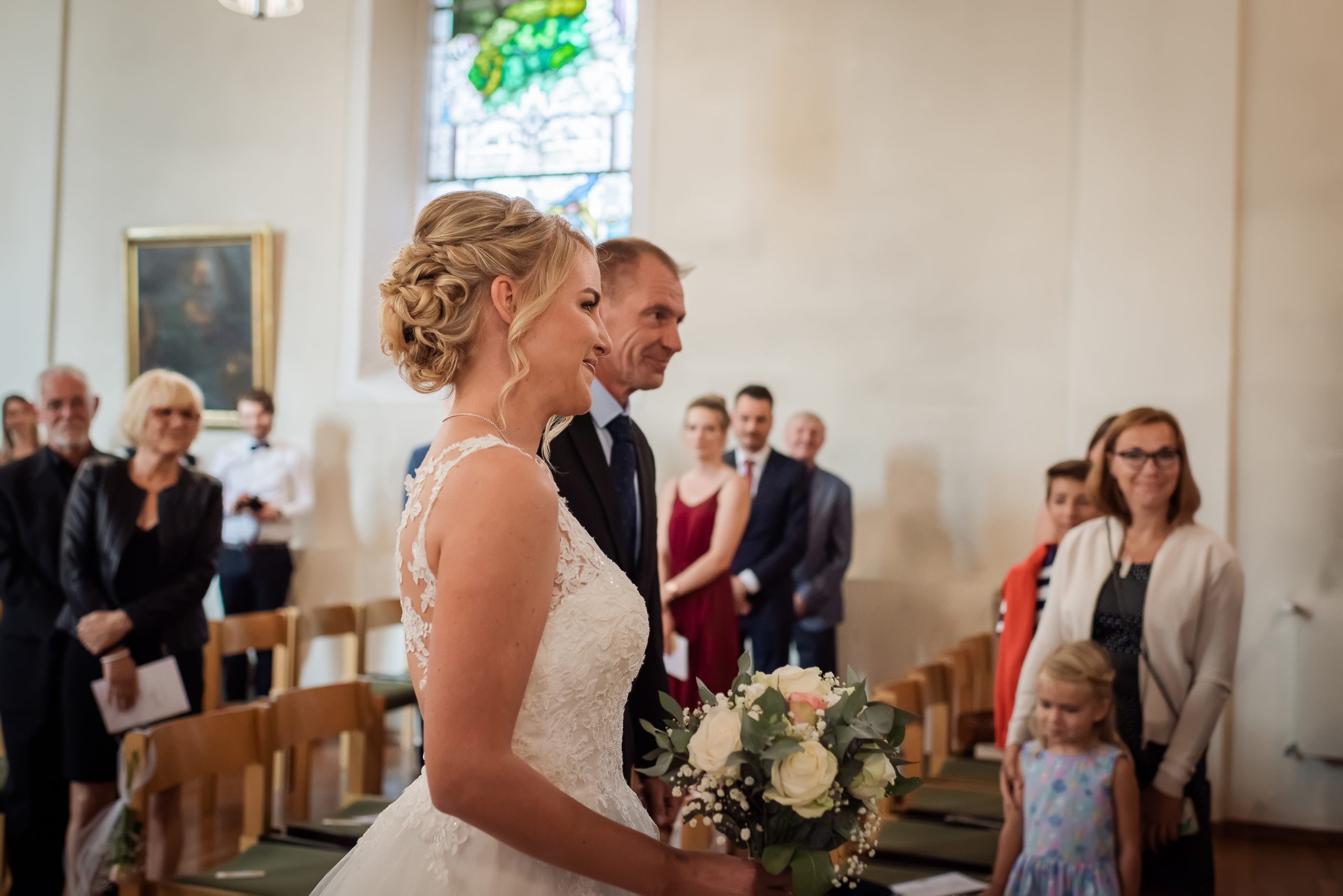 Ein Foto von der Braut, die neben ihrem Vater in Richtung Altar der Kirche läuft, um ihren Bräutigam zu treffen.