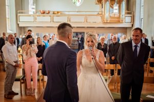 Ein Foto, das den aufregenden Moment zeigt, als die Braut während einer kirchlichen Hochzeit in der Evangelischen Kirche in Friesenheim das Mikrofon übernimmt und einen Überraschungsauftritt für den Bräutigam und alle Gäste gibt.
