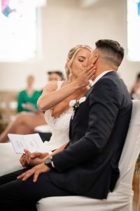 Ein Foto von der Braut, die bei einer kirchlichen Hochzeit in Offenburg sanft das Gesicht des Bräutigams hochhebt, um ihn zu küssen.