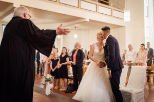 Hochzeitspaar küsst sich nach Segen durch Pfarrer in der Kirche