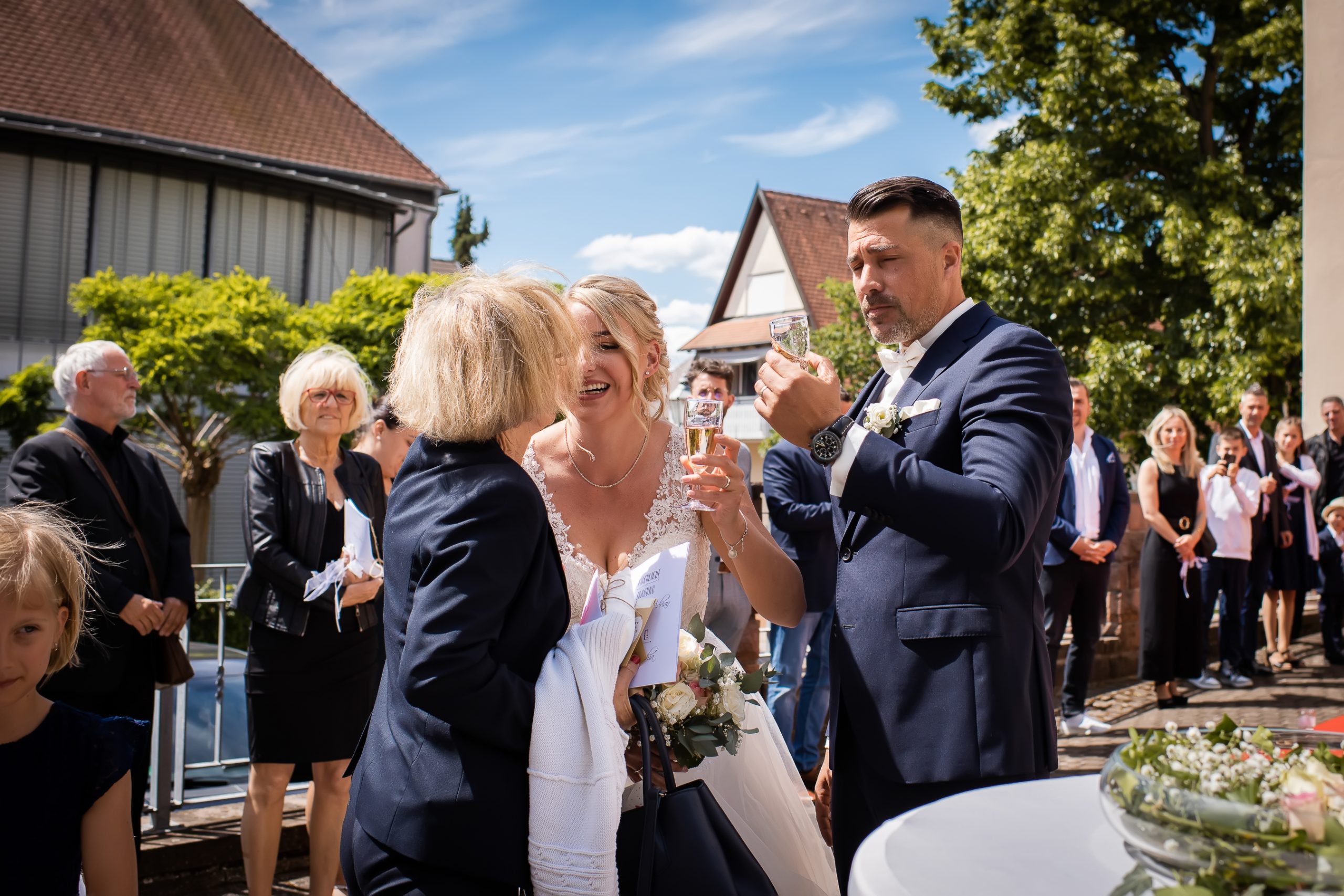 Ein glückliches Brautpaar beim Sektempfang nach ihrer Hochzeit in Friesenheim, von Gästen umgeben.