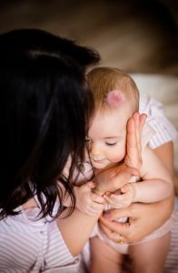 Mutter hält ihr Baby in den Armen und berührt das Gesicht des Babys während Fotoshooting zu Hause in Offenburg.