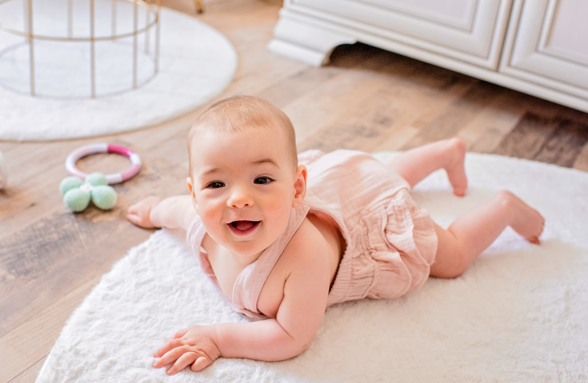 Ein Baby liegt auf dem Bauch auf einem Teppich und lächelt in die Kamera.