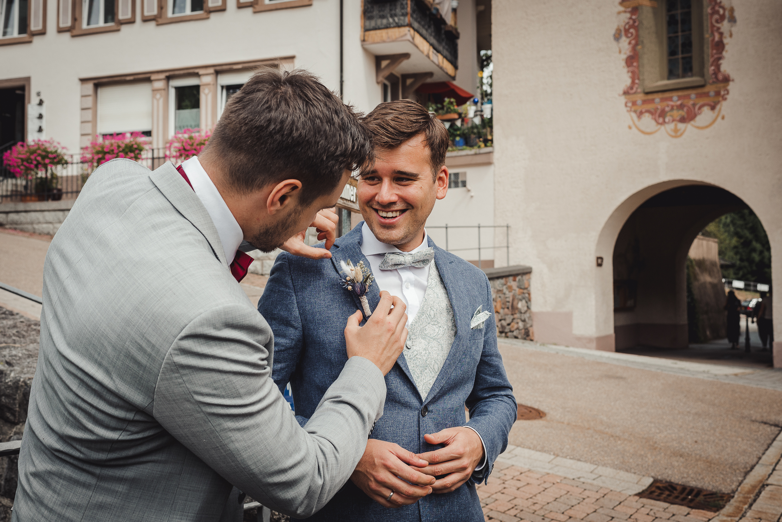 Der Bräutigam lässt sich von einem Hochzeitsgast vor der Kirche in Todmoos den Blumenstrauß im Anzug befestigen