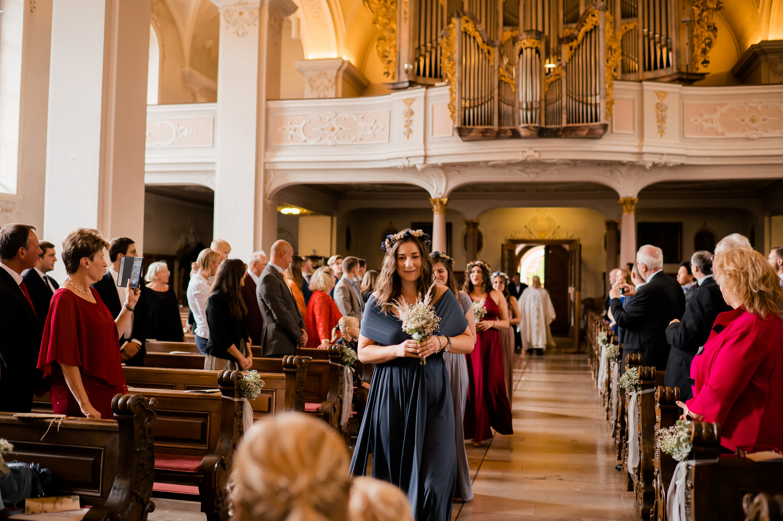 Die besten Freunde der Braut kommen mit einem Blumenstrauß in der Hand in die Wallfahrtskirche Todtmoos, sie tragen schöne Kleider im Boho-Stil.