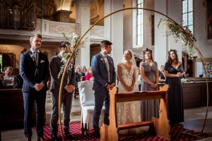 Brautpaar sagt "Ja" vor einem goldenen Hochzeitsbogen im Altar, begleitet von ihren Trauzeugen. Kirchliche Trauung in der Wallfahrtskirche in Todtmoos.