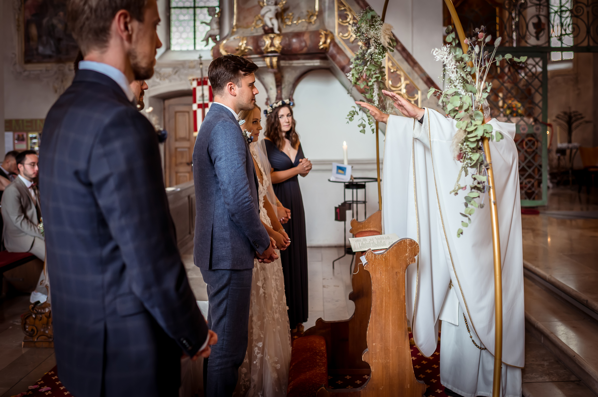 Kirchliche Trauung in einer katholischen Kirche im Schwarzwald, bei der der Pfarrer das Brautpaar neben den Trauzeugen im Altar segnet.