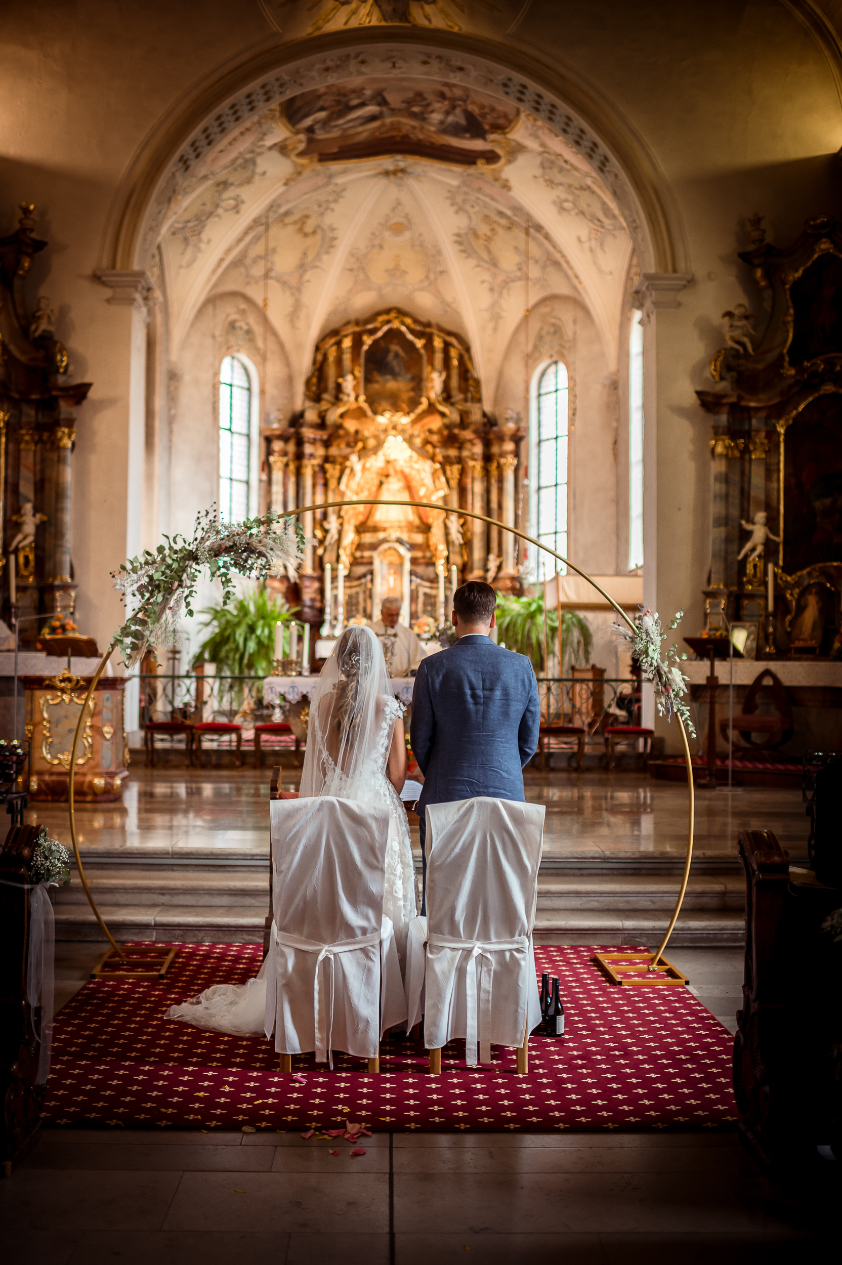 Brautpaar steht von hinten betrachtet vor einem wunderschön dekorierten Altar in der Wallfahrtskirche in Todmoos während ihrer Hochzeit.