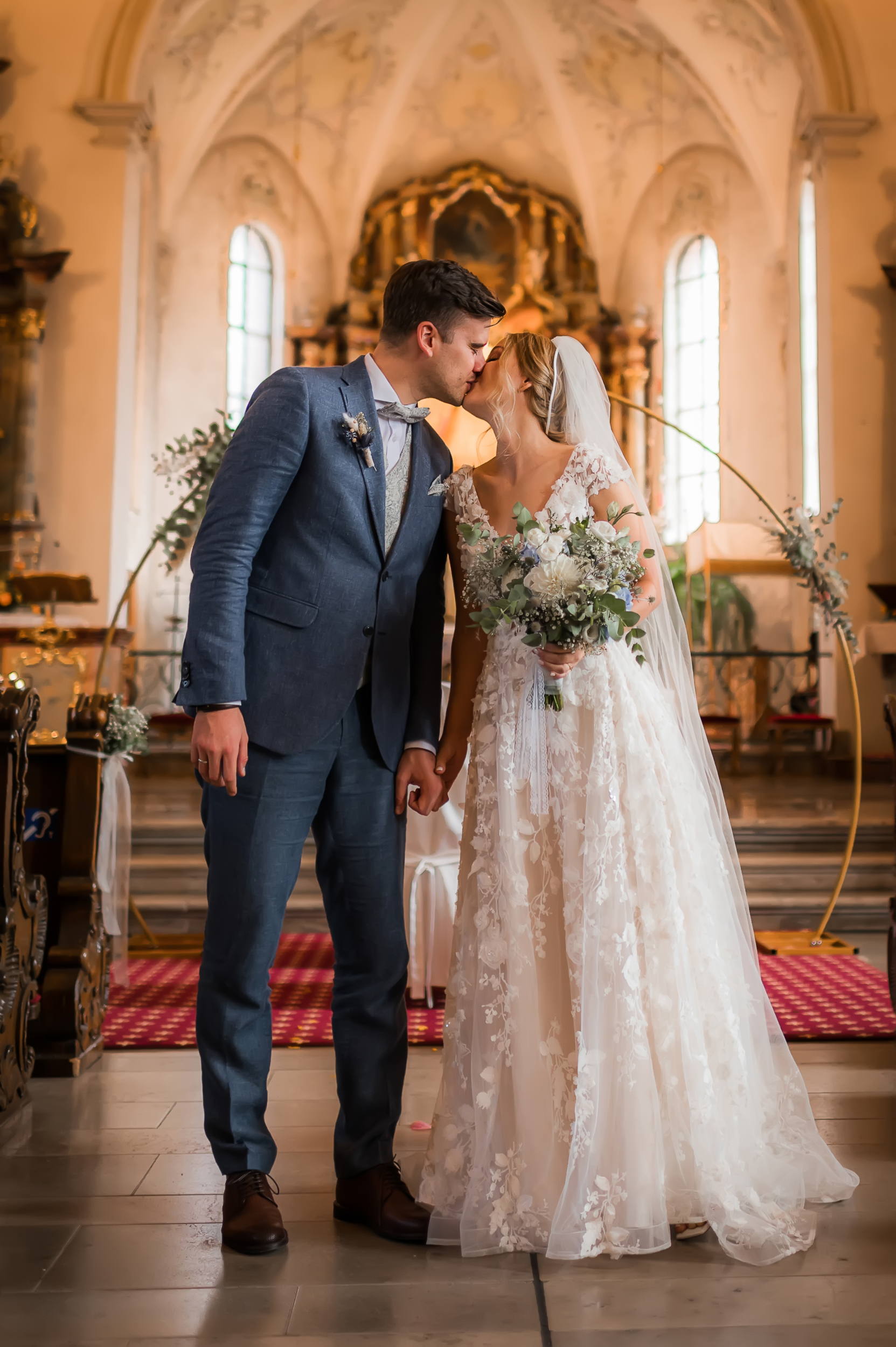Brautpaar verlässt den Altar nach der kirchlichen Trauung und küsst sich vor dem dekorierten goldenen Bogen in der Wallfahrtskirche Todtmoos im Schwarzwald.