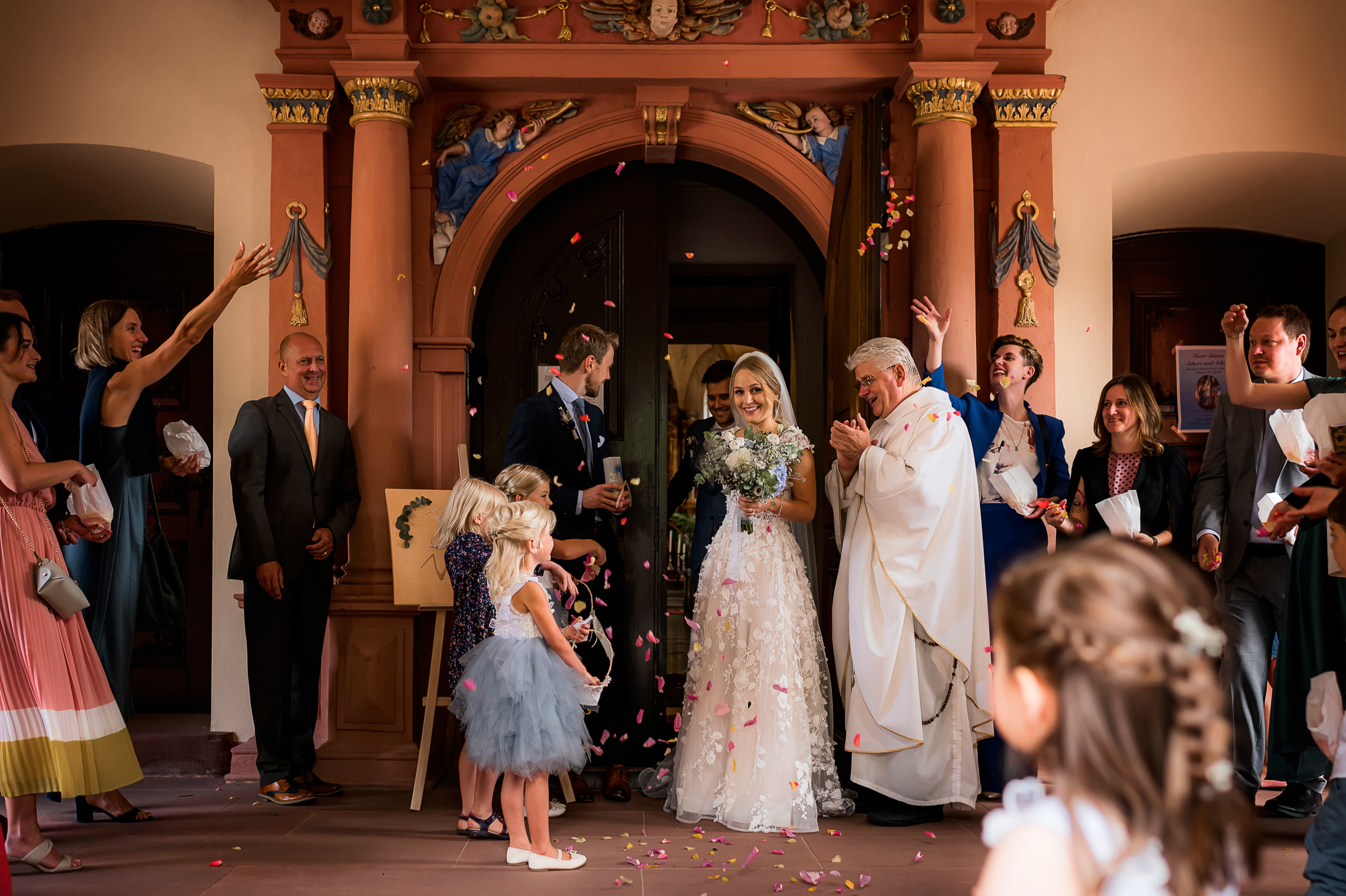 Brautpaar verlässt mit verbundenen Händen die Wallfahrtskirche in Todtmoos, während die Hochzeitsgäste Rosenblüten werfen.