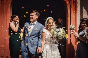 Brautpaar verlässt mit verbundenen Händen die Kirche in Todtmoos, während die Hochzeitsgäste Rosenblüten werfen.