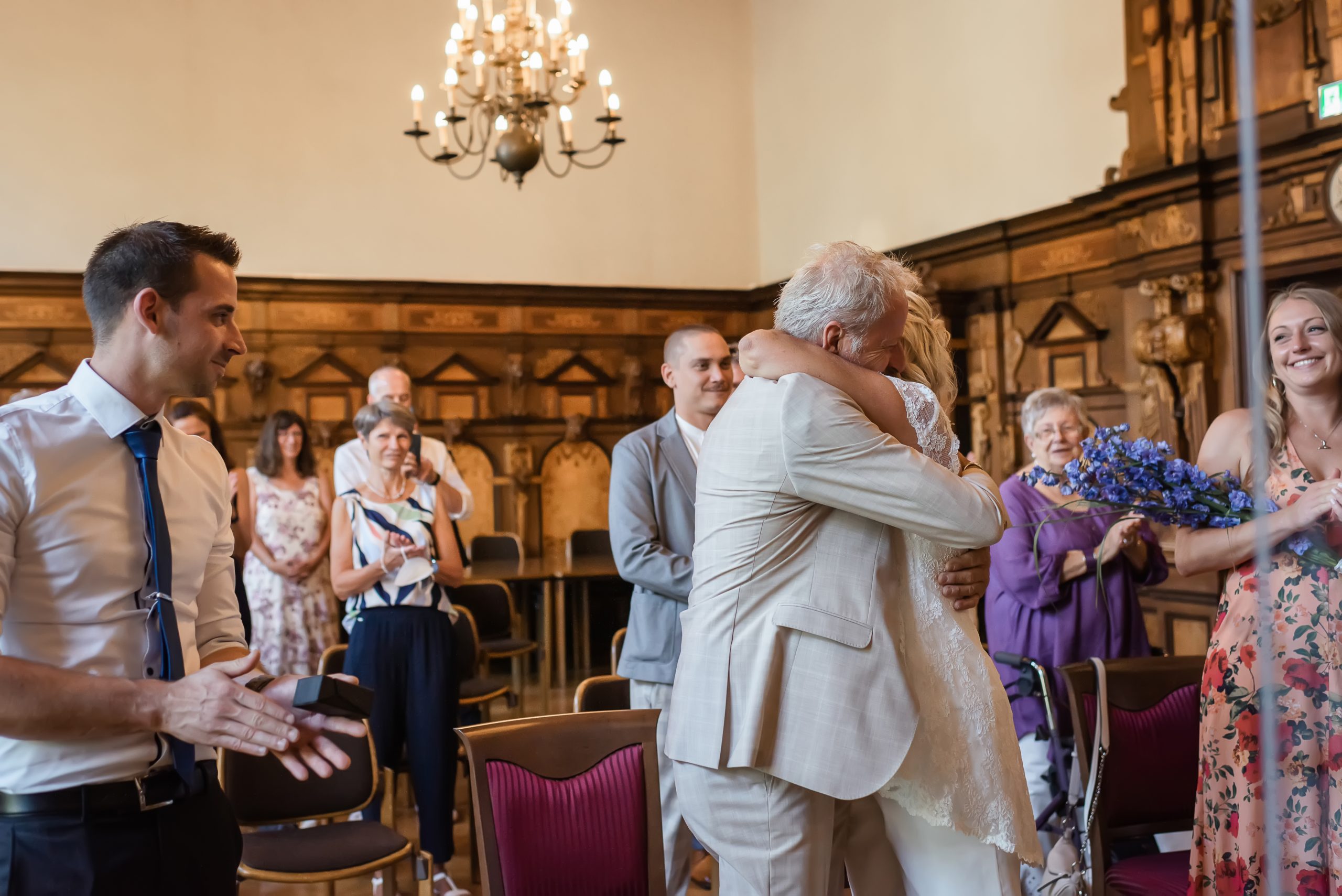 Ein Brautpaar umarmt sich nach der standesamtlichen Trauung im Freiburger Rathaus, während die Gäste applaudieren.