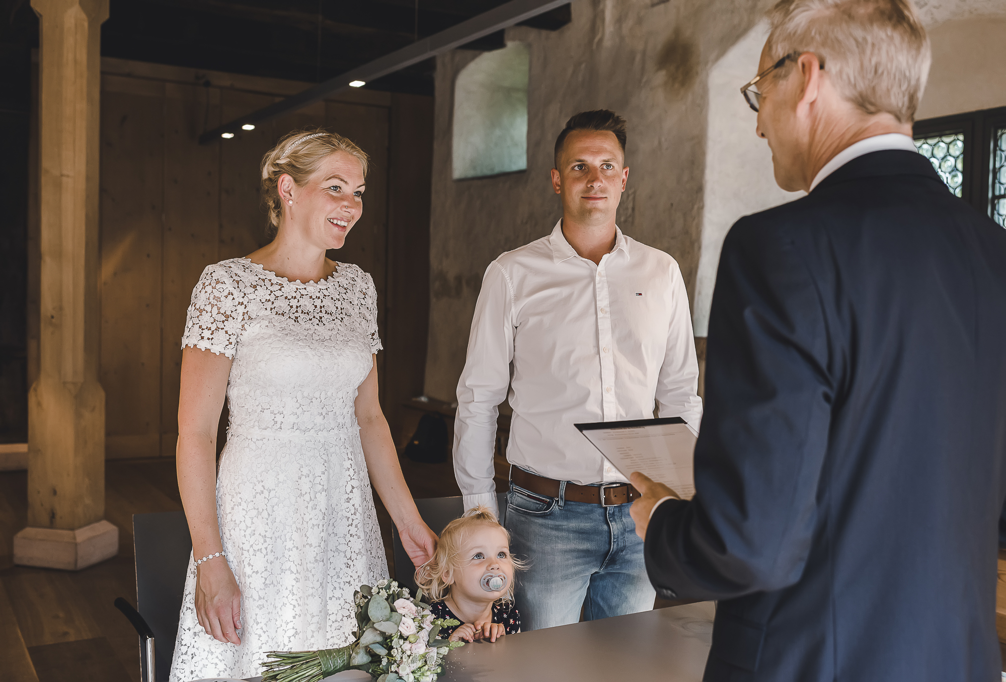 Das frisch verheiratete Brautpaar gibt sich in Kirchzarten das "Ja"-Wort. Inmitten des Standesamts sitzen sie eng umschlungen und strahlen vor Glück. Der Beamte stellt ihnen die Fragen und die kleine Tochter schaut neugierig in die Mitte. Ein magischer Moment, den die talentierte Hochzeitsfotografin Isabela Campos für immer festgehalten hat.