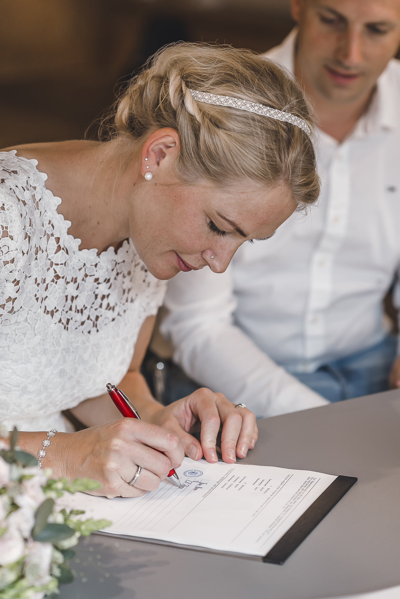 In diesem beeindruckenden Foto wird die emotionale Unterzeichnung der offiziellen standesamtlichen Eheschließung im Schwarzwald eingefangen. Die Braut unterzeichnet das Dokument mit Ernsthaftigkeit und Konzentration, während der Bräutigam sie voller Liebe und Bewunderung ansieht. Die Fotografin Isabela Campos fängt die Stimmung und das Gefühl dieses besonderen Augenblicks perfekt ein.