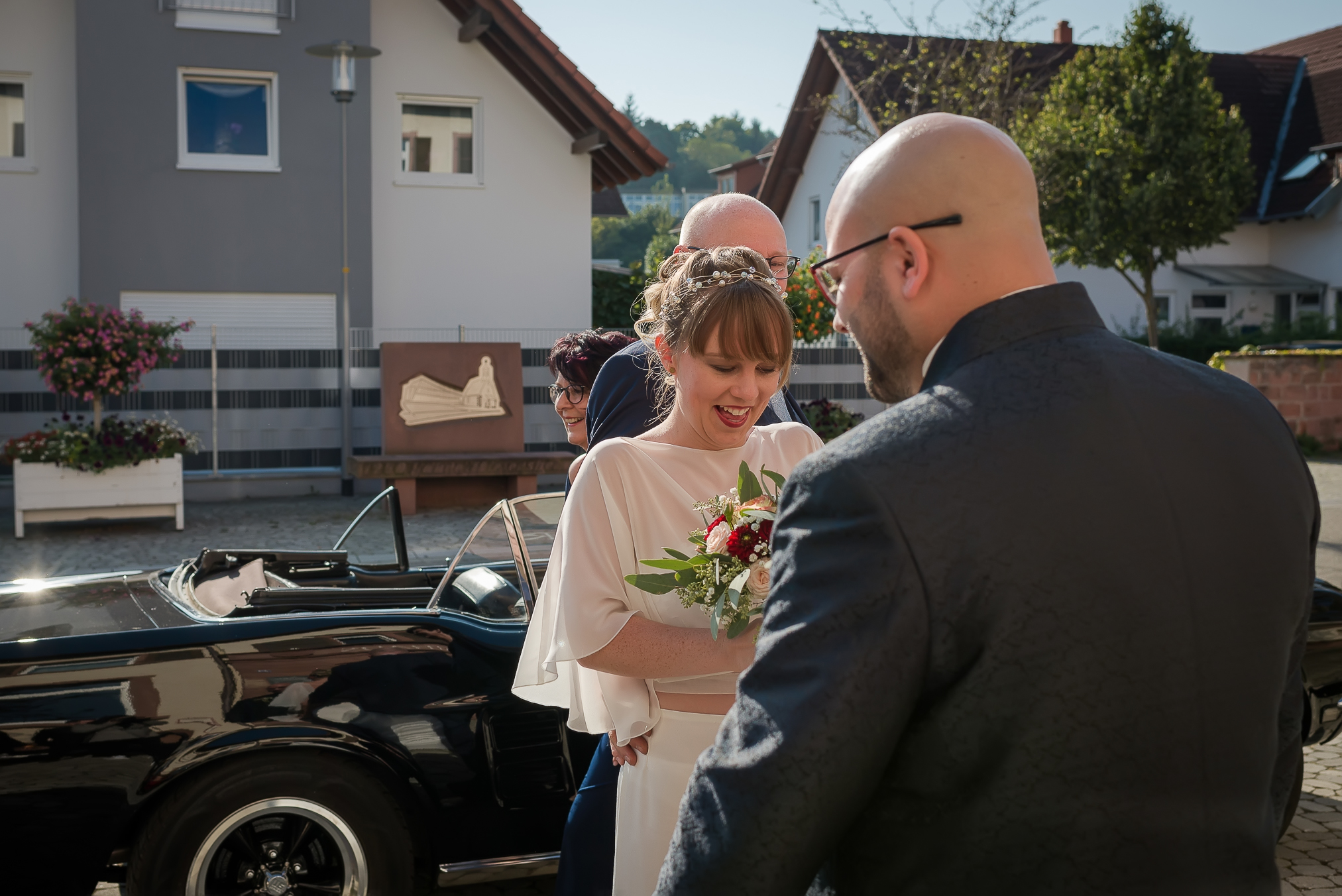 Eine Braut steigt aus einem Oldtimer vor dem Rathaus in Mietersheim für ihre standesamtliche Trauung aus und wird vom Bräutigam erwartet.