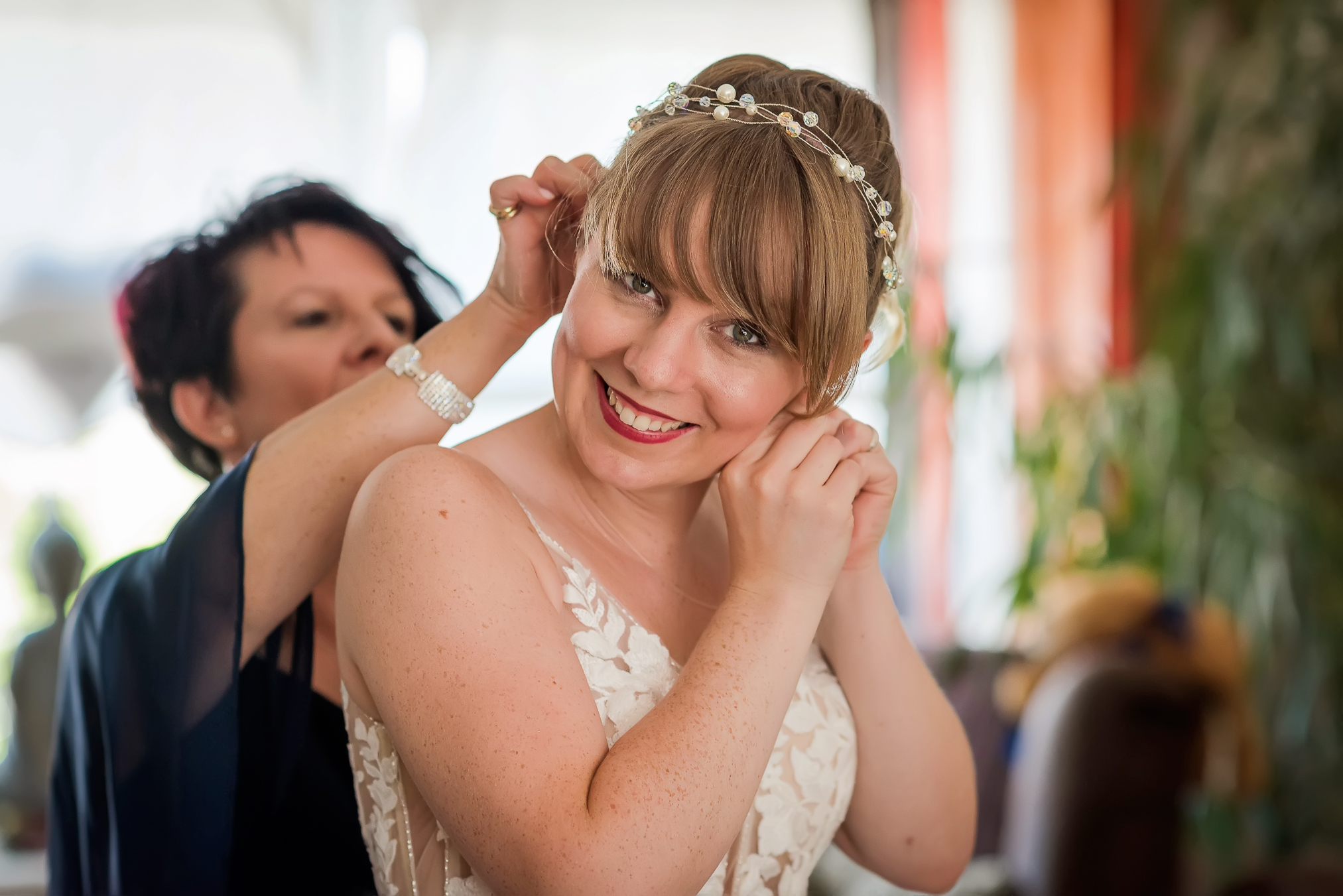 Die Braut wird von ihrer Mutter unterstützt, während sie ihre Hochzeitsohrringe anlegt und in die Kamera der Hochzeitsfotografin Isabela Campos lächelt.