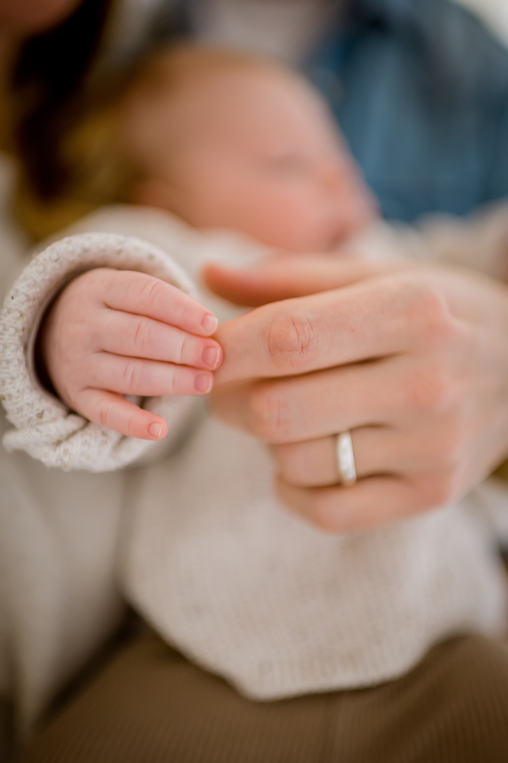 Detailaufnahme der Hand eines Babys, das den Zeigefinger seiner Mutter umklammert.