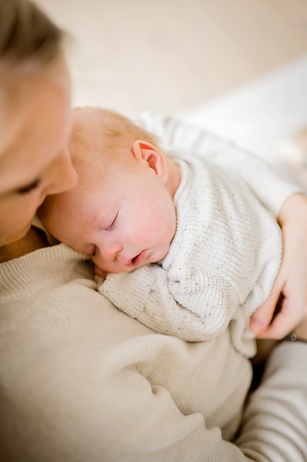 Eine junge Mutter, die ihr Baby in ihrem Schoß hält und liebevoll in ihre Arme schaut, während ihr Baby friedlich schläft.