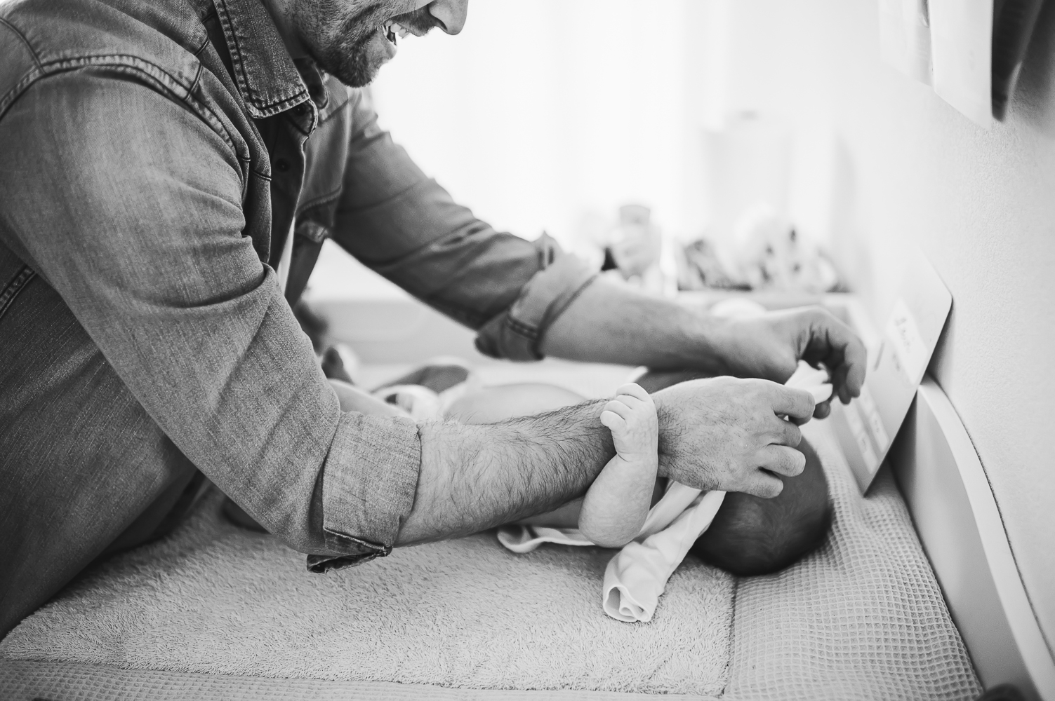 Ein Nahaufnahme-Porträt eines stolzen Vaters, der die Kleidung seines Babys wechselt, während das Baby auf dem Wickeltisch liegt.