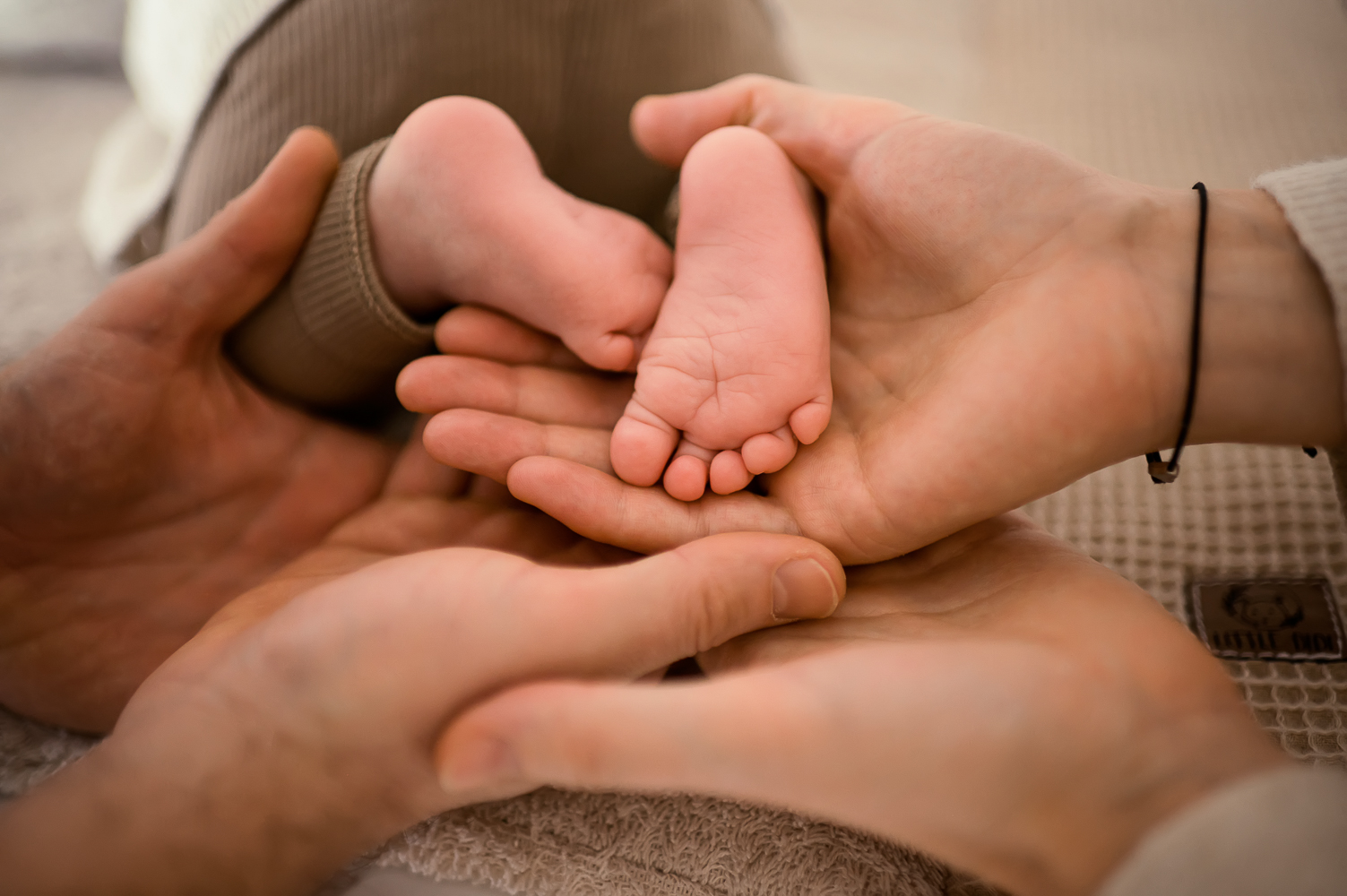Ein Detailfoto der winzigen Füße eines Babys auf einem Wickeltisch, umgeben von den Händen der Eltern.