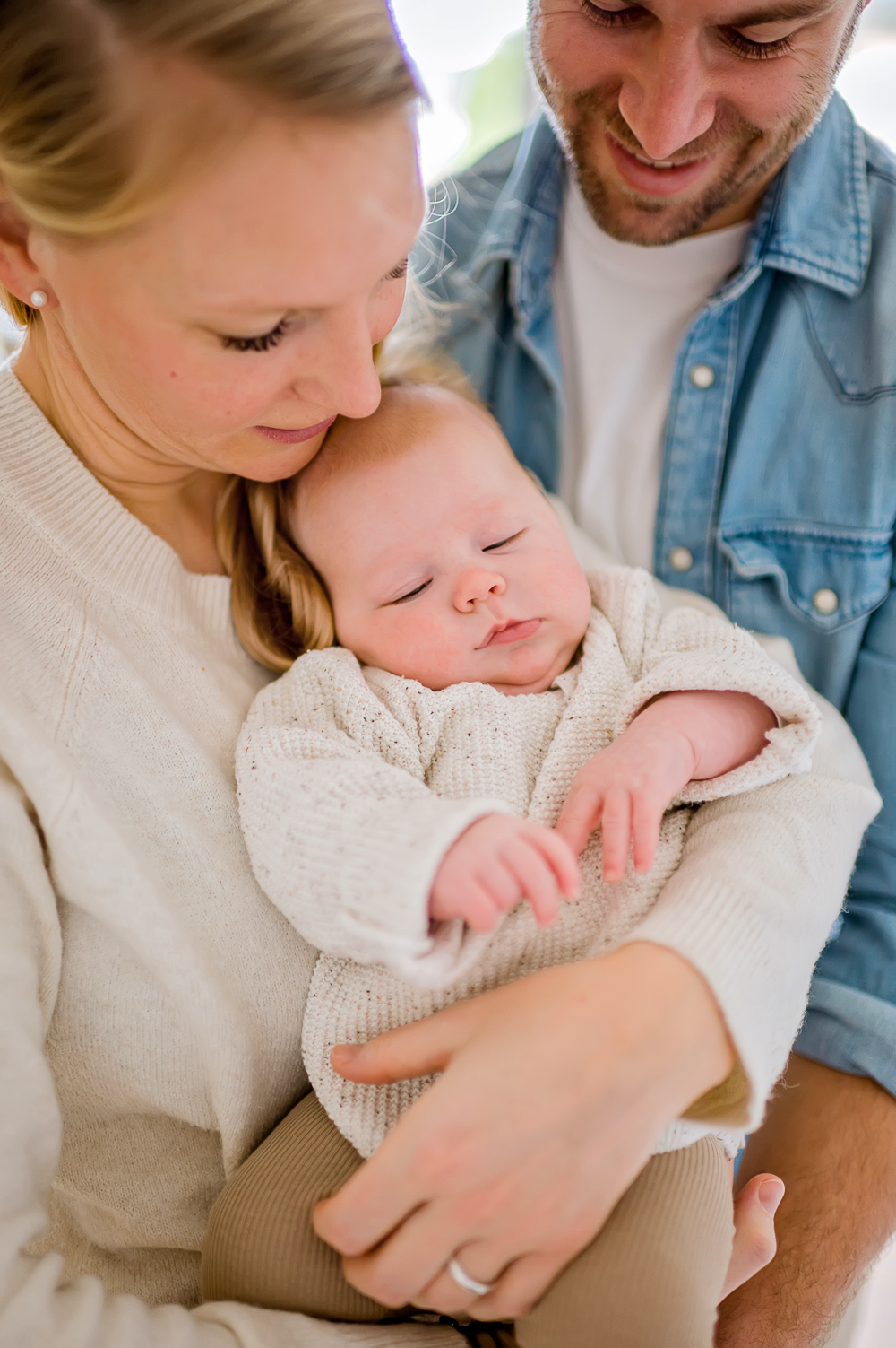 Eine junge Mutter und ein Vater umarmen sich mit ihrem Baby im stilvollen Familienfotoshooting zu Hause.