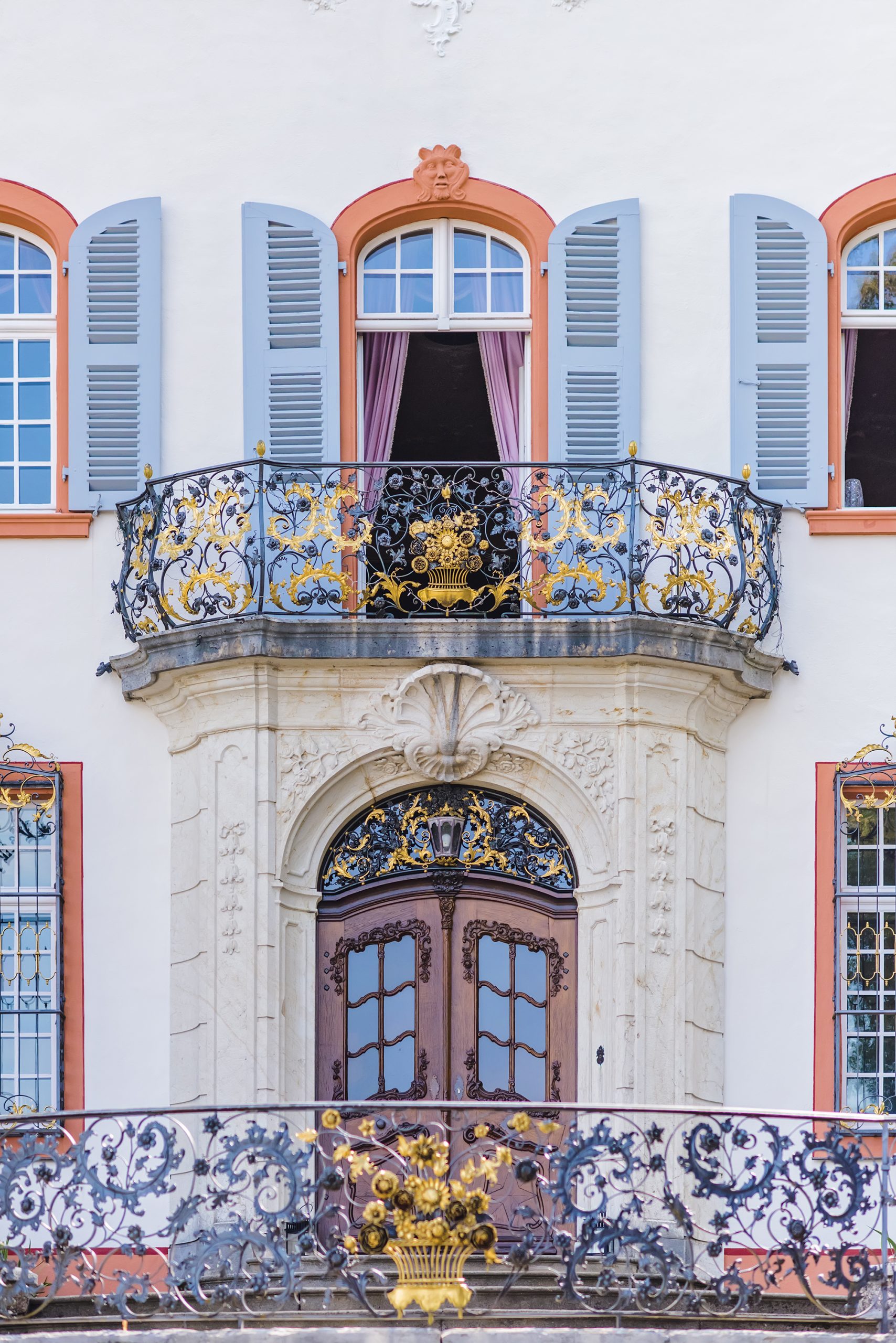 Ein Detailfoto der Fassade des Schlosses Burgeln in Schliengen, mit besonderem Fokus auf der oberen Balkon mit Geländern und Fenstern.