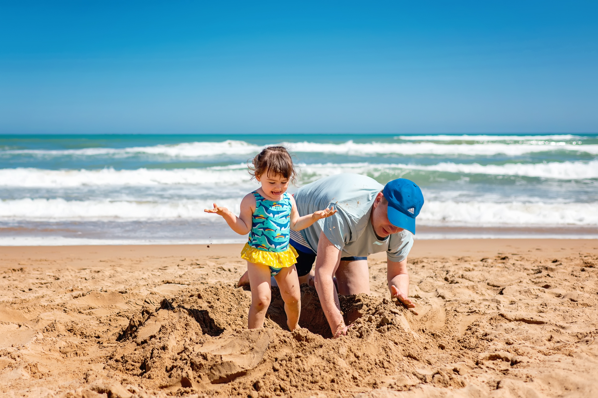 Natürliches Strandfotoshooting mit kleinem Mädchen und Vater, die Sandburg bauen